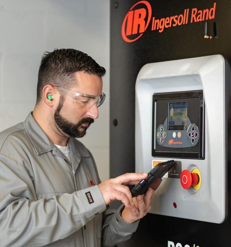 Man in safety gear using a touch screen control panel on an Ingersoll Rand industrial machine.